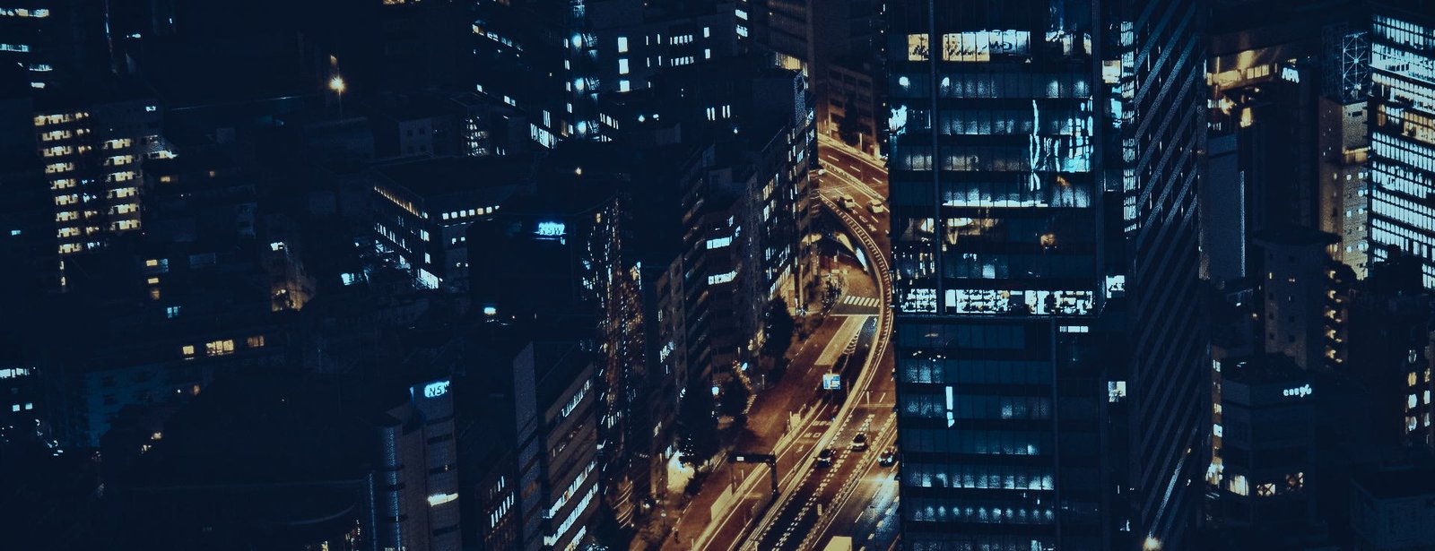 Avenida elevada iluminada cruzando entre torres corporativas de noche, vista a&eacute;rea
