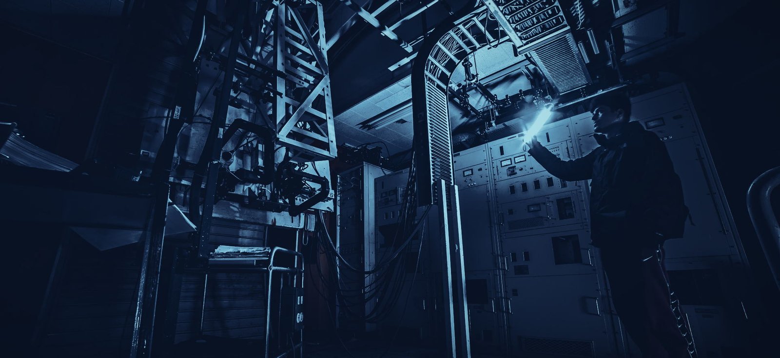 Ingeniero de ANI revisando con linterna un tablero de control en una planta a media luz